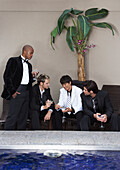 Männer in Abendgarderobe trinken Cocktails am Pool
