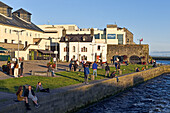 Junge Leute sitzen am Ufer der Mündung des Corrib-Flusses, Innenstadt von Galway, Connemara, County Galway, Connacht, Republik Irland