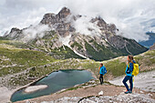 Hikers on path overlooking the Lago dei Piani inferiore, Three Peaks Nature Park, Dolomites, South Tyrol, Italy