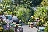 Üppig bepflanzte Terrasse mit Sitzplatz und Rosen, Schafgarbe, Erdbeere, Hortensie, Salbei, Grasnelke,  Lavendel, Rosmarin, Gräser in Töpfen