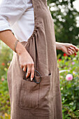 Gärtnerin im Leinenkleid mit Schere in der Tasche im Garten