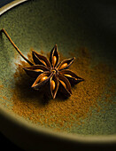 Star anise on ground aniseed powder in a green bowl