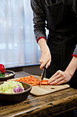 Woman cuts carrots into cubes for fresh vegetable dish