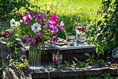 Strauß mit Kosmeen (Cosmos) im sommerlichen Garten mit Krug mit Beerenwasser