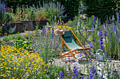 Deckchair between delphinium (Delphinium) and dyer's chamomile (Anthemis tinctoria) in the summer garden