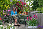 Frau macht Fussbad mit Rosenblüten auf Terrasse, Blumentöpfe mit Dahlien (Dahlia), Lupinen (Lupinus), Schafgarbe, Weigelia, Fächerahorn