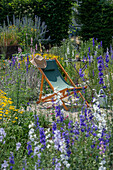 Deckchair between delphinium (Delphinium) and dyer's chamomile (Anthemis tinctoria) in the summer garden