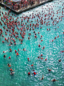 Aerial view of crowd with swimmers wearing red caps in turquoise water,Boca Gentil,Curacao