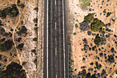 Luftaufnahme einer rissigen Straße, die sich durch eine karge Wüste mit verstreuten Büschen windet, Arizona, Vereinigte Staaten