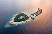 Luftaufnahme der Bungalows eines Luxusresorts entlang des Riffs bei Sonnenuntergang auf der Insel Fesdhoo auf den Malediven