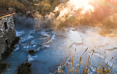 Luftaufnahme der heißen Quelle Terme di Saturnia mit nebligem Dampf und historischem Steingebäude, Toskana, Italien