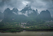 Luftaufnahme des Guilin-Gebirges mit einem ruhigen Fluss und einem malerischen Dorf, Kreis Yangshuo, Volksrepublik China