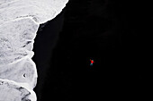 Luftaufnahme von schwarzem Strand, einer Person, Wellen und Eis in Reynisfjara, Island