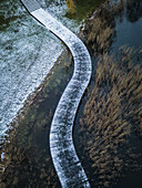 Aerial view of a serene foot bridge over frozen water surrounded by snow and reeds,Trakai,Lithuania