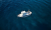 Aerial view of a little fishing boat at dawn surrounded by a crystalline deep blue sea moored in Calabria,Italy