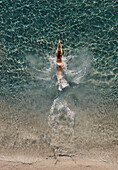 Aerial view of a stunning woman wearing a white bikini while having fun diving into a transparent sea in Montepaone,Calabria,Italy