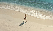 Aerial view of a beautiful blonde girl strolling by the sea and gazing at the amazingly turquoise waters in San Sostene,Calabria,Italy