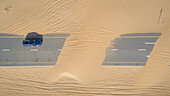Luftaufnahme eines Autos, das auf einer mit Sand bedeckten Straße in der Wüste von Dubai fährt,V.A.E