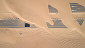 Luftaufnahme eines Autos, das auf einer mit Sand bedeckten Straße in der Wüste von Dubai fährt,V.A.E