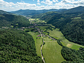 Luftaufnahme eines malerischen Tals mit einem beschaulichen Dorf, üppigen Feldern und majestätischen Bergen, Kruth, Frankreich