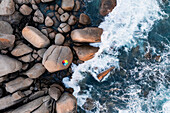 Aerial view of waves crashing on rocks with umbrella and boulders,Clifton,Cape Town,South Africa
