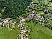 Luftaufnahme eines charmanten Dorfes mit üppigen Feldern und einer kurvenreichen Straße, umgeben von bewaldeten Hügeln, Kruth, Frankreich