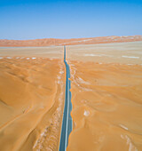 Luftaufnahme einer leeren, geraden, mit Sand bedeckten Straße in der Wüste von Abu Dhabi,V.A.E