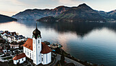 Aerial view of the tranquil Lake Lucerne in Switzerland. Image features a traditional catholic swiss church that overlooks the nearby mountain ranges