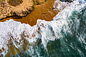 Aerial view of the ocean at the shore of the boardwalk,rough waves with a lot of foam hitting the rocks