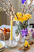 Österlich dekorierter Tisch mit Kerze, Weidenkätzchen, Narzissen und Krokussen