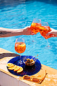 Two people drinking Aperol Spritz by the pool