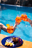 Two people drinking Aperol Spritz by the pool