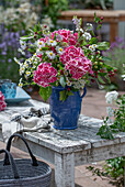 Blumenstrauß mit Hortensie, Zierapfel, Berufkraut (Erigeron 'Sommerneuschnee'), Mutterkraut und Giersch im Krug auf dem Gartentisch