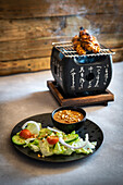 Chicken satay on a table grill with peanut sauce and salad