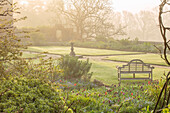 Frühlingsgarten mit Tulpen, Lutyens Bank und Sonnenuhr aus Stein im Morgennebel