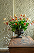 Tulpen in Metallgefäß auf Holztisch vor verzierter Tapete