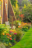 Frühlingsgarten mit Tulpenbeeten und weißer Bank am Backsteinhaus