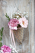 Florales Arrangement aus Nelke und Schleierkraut im Drahtkegel an Holzwand