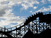 Silhouette von Menschen, die ihre Hände auf einer Achterbahn heben.