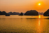 Ha Long Bay, Vietnam. Landscape view of boat carrying tourists at sunset through the limestone karsts and islets of the UNESCO Heritage Site.