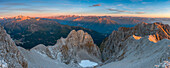 Sonnenaufgang im Gebirge, der die Gipfel des Adamello-Brenta-Parks beleuchtet, von einem Gipfel in den Brenta-Dolomiten aus gesehen, über dem Tovel-See in der Provinz Trient, Region Trentino-Südtirol, Italien.