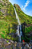 Man admiring the waterfall of Poco do Bacalhau at the sun light in Faja Grande, Lajes das Flores municipality, Flores Island (Ilha das Flores), Azores archipelago, Portugal, Europe