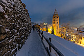 Church of Saint Pantalon and snow covered town centre and mountainous background in winter at dusk, Courmayeur, Aosta Valley, Italian Alps, Italy