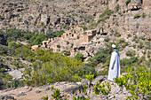Mann in Dishdasha bewundert altes Lehmdorf in den Ruinen von Al Ain, hochgelegene Dörfer des Jabal Al Akhdar (Grüne Berge) um das Sayq-Plateau, Oman