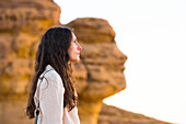 Woman in front of Face Rock, a sandstone rock formation in shape of human head profile, Hegra, UNESCO, AlUla, Medina Province, Saudi Arabia