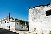A person walks near the white walls of a winery in the Barrio Alto of Sanlucar de Barrameda, surrounded by sunny blue skies.