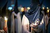 Nazarenos shielding candle flames from wind during a religious procession in Holy Week.