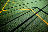 Soccer ball resting on a green outdoor field with sunlight creating shadows.