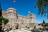 Visitors admire the historic Santiago Castle in Sanlucar de Barrameda, Spain, against a clear blue sky and vibrant greenery.