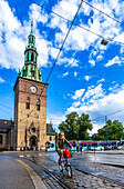 Oslo, Norwegen, 10. August 2017, Eine Person radelt an der Kathedrale von Oslo vorbei und genießt das sonnige Wetter, umgeben von leuchtenden Wolken und dem Stadtleben auf einer belebten Straße.